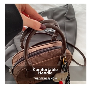 Details der braunen Wildledertasche mit Plüsch-Anhänger und glatten Zylinder-Griffen