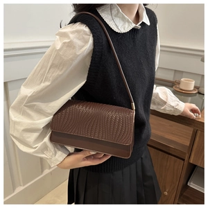 Detailed view of dark brown shoulder bag featuring woven texture and smooth leather finish