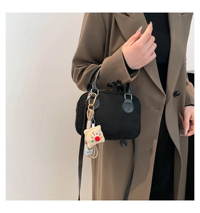 Detail of black velvet pillow bag with cute plush pendant and slim leather shoulder strap
