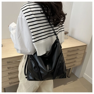 Detail view of the black oversized tote bag with functional zippers on soft leather surface