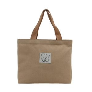Minimalist khaki canvas bucket handbag with brown woven handles and a cute bear patch