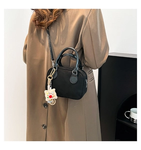 Detail of a black crossbody pillow bag with a plush charm and detachable shoulder strap