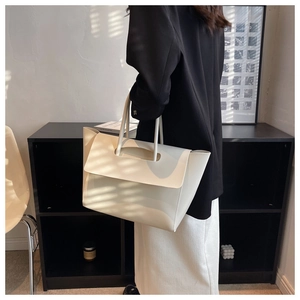 Detail of minimalist cream tote bag showing unique curved handle and matte leather texture