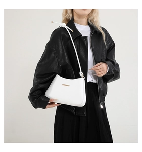 Détail d'un sac sous les bras en cuir blanc brillant avec logo doré et bandoulière nouée