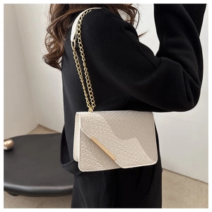 Detail of white woven square bag featuring a gold chain strap and metal trim on flap