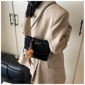 Close-up of black quilted hobo bag with gold chain and plush bear charm on model