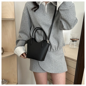 Close-up of matte black bucket bag with adjustable strap worn on a casual grey outfit