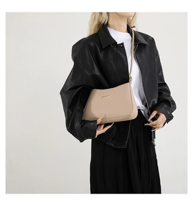 Detail of elegant beige baguette bag with gold metal bar on a black leather jacket