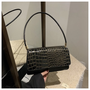 Detail of black glossy baguette bag featuring gold crocodile embossed flap and metal buckle