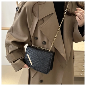 Detail of black woven leather handbag with gold chain strap and metallic closure clasp