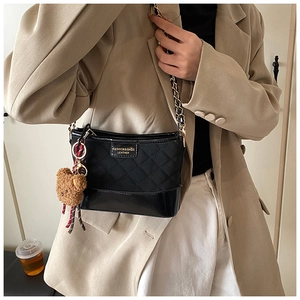 Close-up of black quilted shoulder bag with gold chain and plush bear charm