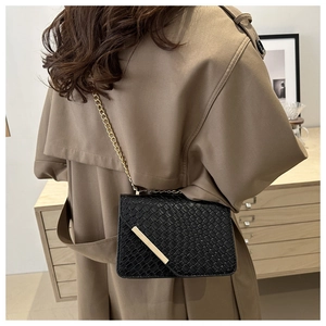 Detail of black woven crossbody bag with gold chain strap on khaki trench coat