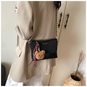 Quilted black crossbody bag with gold chain strap and cute bear pendant on a model