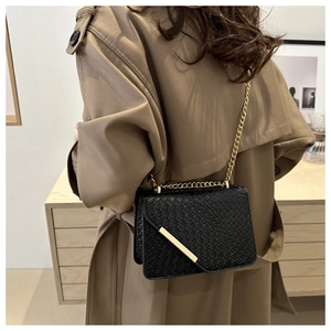 Détail d'un sac bandoulière noir tissé avec boucle dorée porté sur un trench-coat kaki
