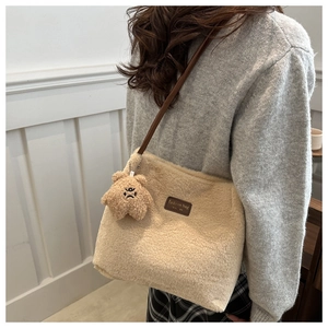 Close-up of beige plush tote bag featuring a leather patch and angry bear pendant charm