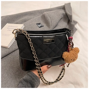 Detail of black quilted shoulder bag featuring metal chain and brown teddy bear charm