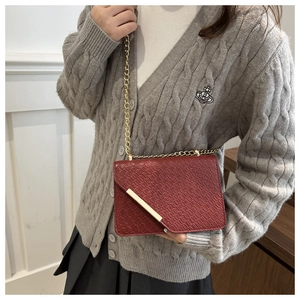 Detail of burgundy crocodile-embossed leather flap bag with gold chain and metal accent