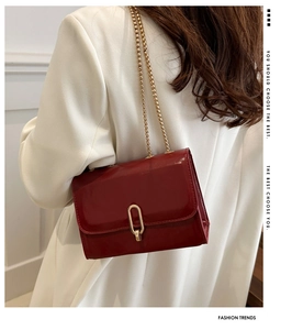 Side view of a glossy wine red chain shoulder bag worn with a white blazer
