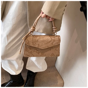 Detail of elegant lotus and koi embossed leather on a beige shoulder bag with braided handle