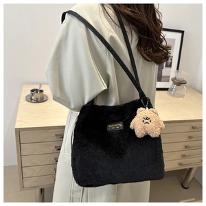Close-up of black plush tote bag with fashion label and cute teddy bear pendant charm
