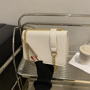 White woven texture crossbody bag with gold chain strap displayed on a modern metal shelf