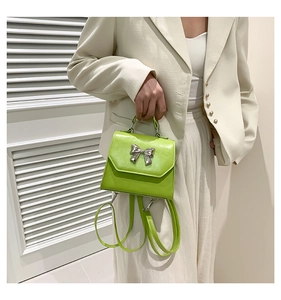 Detail of a shiny green mini bag with silver bow decoration and slender strap