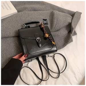 Dettaglio zaino vintage in pelle cerata con ciondolo a campanella dorata su cappotto