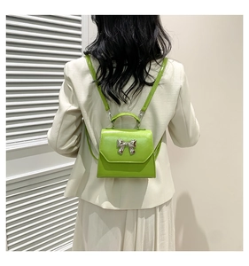 Green mini backpack with silver bow buckle worn on model's back for fashion display