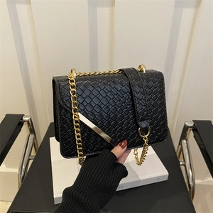Black woven texture crossbody bag with gold chain strap shown in a modern studio setting