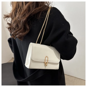 Detail of white glossy square shoulder bag with gold clasp on black coat for contrast