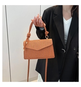 Detail of a brown woven straw handbag with knotted handles and textured envelope flap