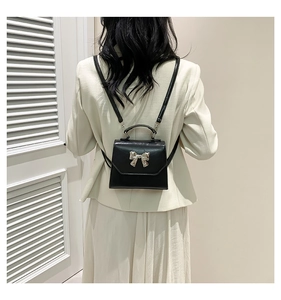 Detailed view of black mini crossbody bag with silver bow buckle on model outfit