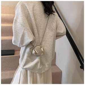 Silver fish-shaped metallic crossbody bag with chain strap worn by a model on stairs
