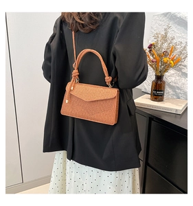 Detailed back view of a burnt orange woven crossbody bag with a knotted top handle