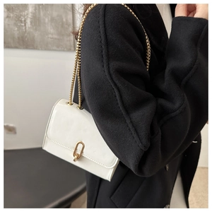 Close-up of a white patent leather square bag with a gold buckle and chain strap
