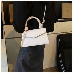 Détail de la texture florale embossée blanche sur un sac trapèze avec ferrures dorées