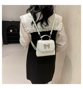 Rear view of model wearing a white mini backpack with a silver bow knot decoration