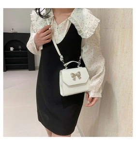 Detail of a creamy white mini crossbody bag with a metal bow and leather texture
