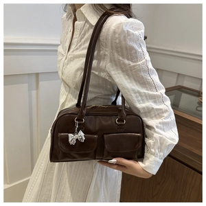 Dettaglio borsa bowling marrone scuro con tasche frontali e ciondolo fiocco argento