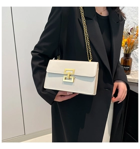 Sac à bandoulière en cuir blanc avec fermoir doré et chaîne sur un blazer noir élégant