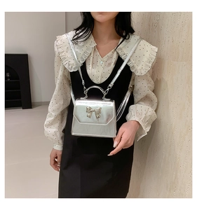 Detail of silver metallic crossbody bag with fixed handle and metallic bow accent