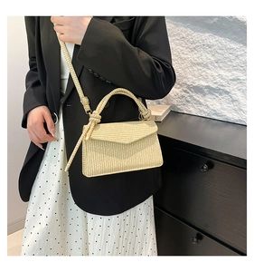 Detail of beige straw woven crossbody bag featuring knot handle and textured envelope flap