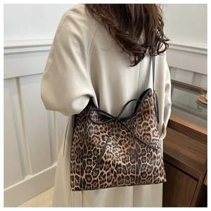Close-up of leopard print tote bag with black leather bow detail on model in beige coat