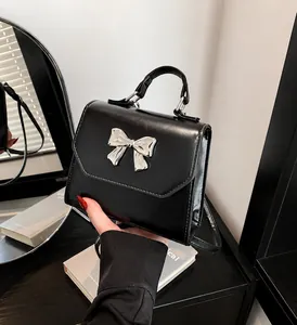 Detail of black leather square handbag with silver bow hardware and top handle strap