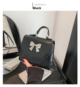 Detail of black leather square handbag with silver bow hardware and top handle strap