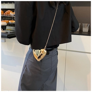 Détail macro d'une pochette dorée en forme de cœur avec design facetté et chaîne en or fin