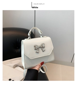 Detail of white leather mini bag featuring a silver bow buckle and elegant top handle