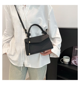 Detail of black woven texture crossbody bag with gold hardware and top handle