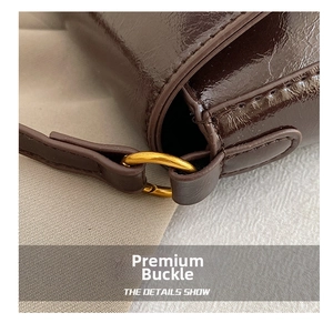 Detail of dark coffee patent leather saddle bag featuring golden metal rings and fine stitching