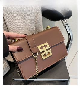 Détail d'un sac bandoulière marron foncé avec fermoir géométrique doré et bandoulière chaîne